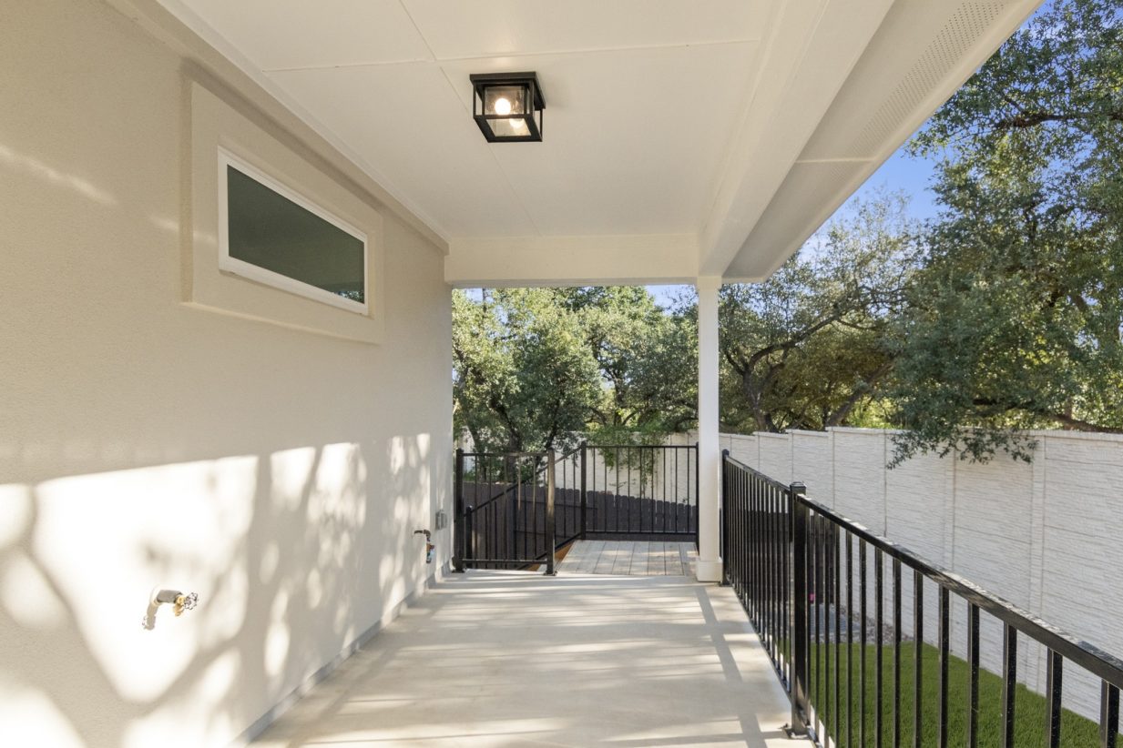 Image of back exterior of a brick one story home with a back covered porch leading to a backyard with greenery