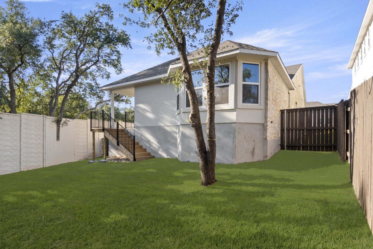 Image of the back exterior of a brick one story home with a back yard and brown wooden fence