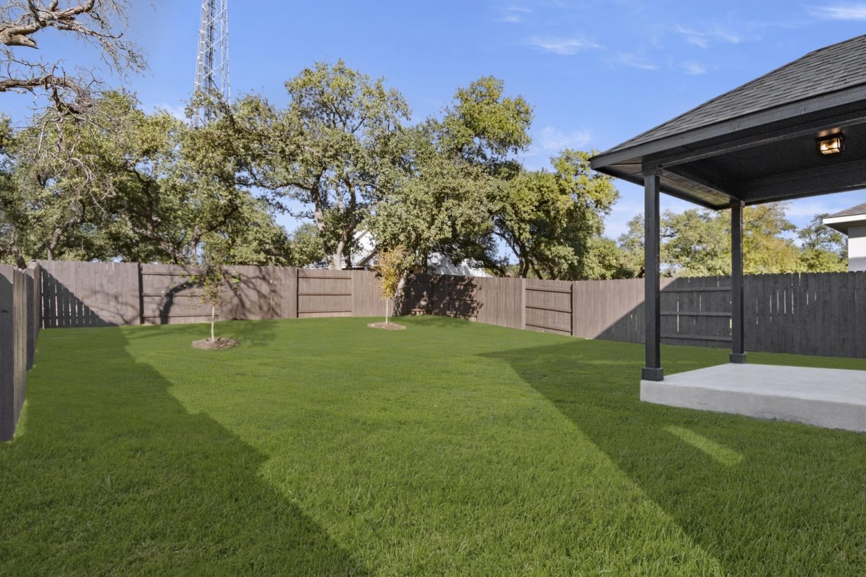Image of the backyard of a two story home with a covered porch and green grass with a