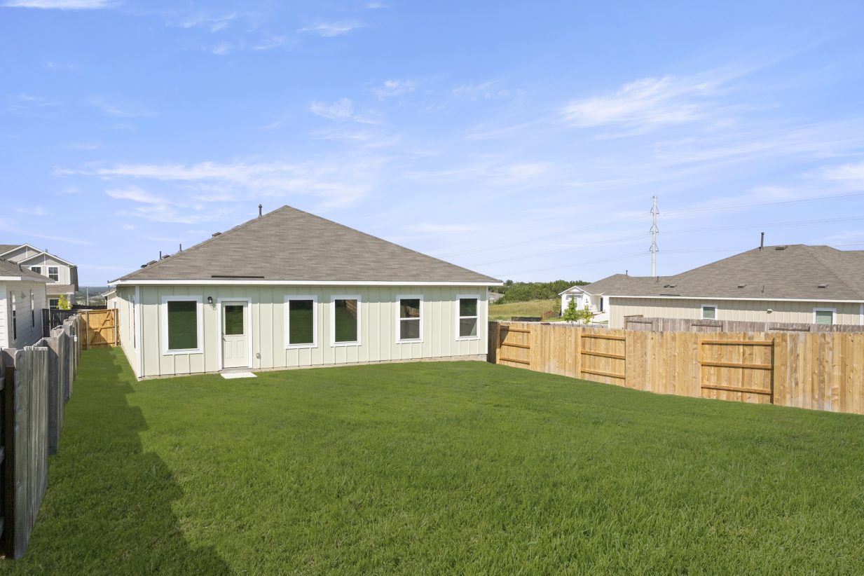 Image of one-story grey-green home rear exterior with backyard grass, wood fence, and sky