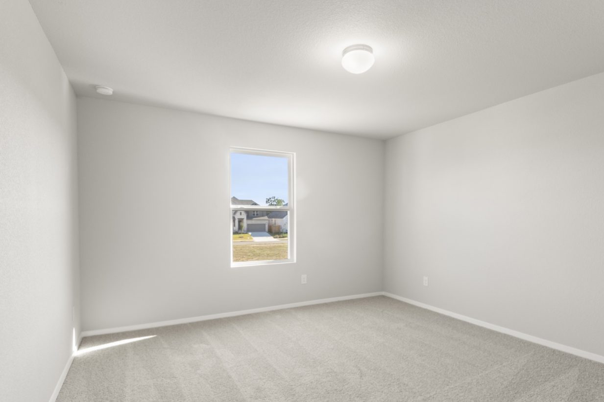 Image of a bedroom with tan carpeting and light grey painted walls with a window