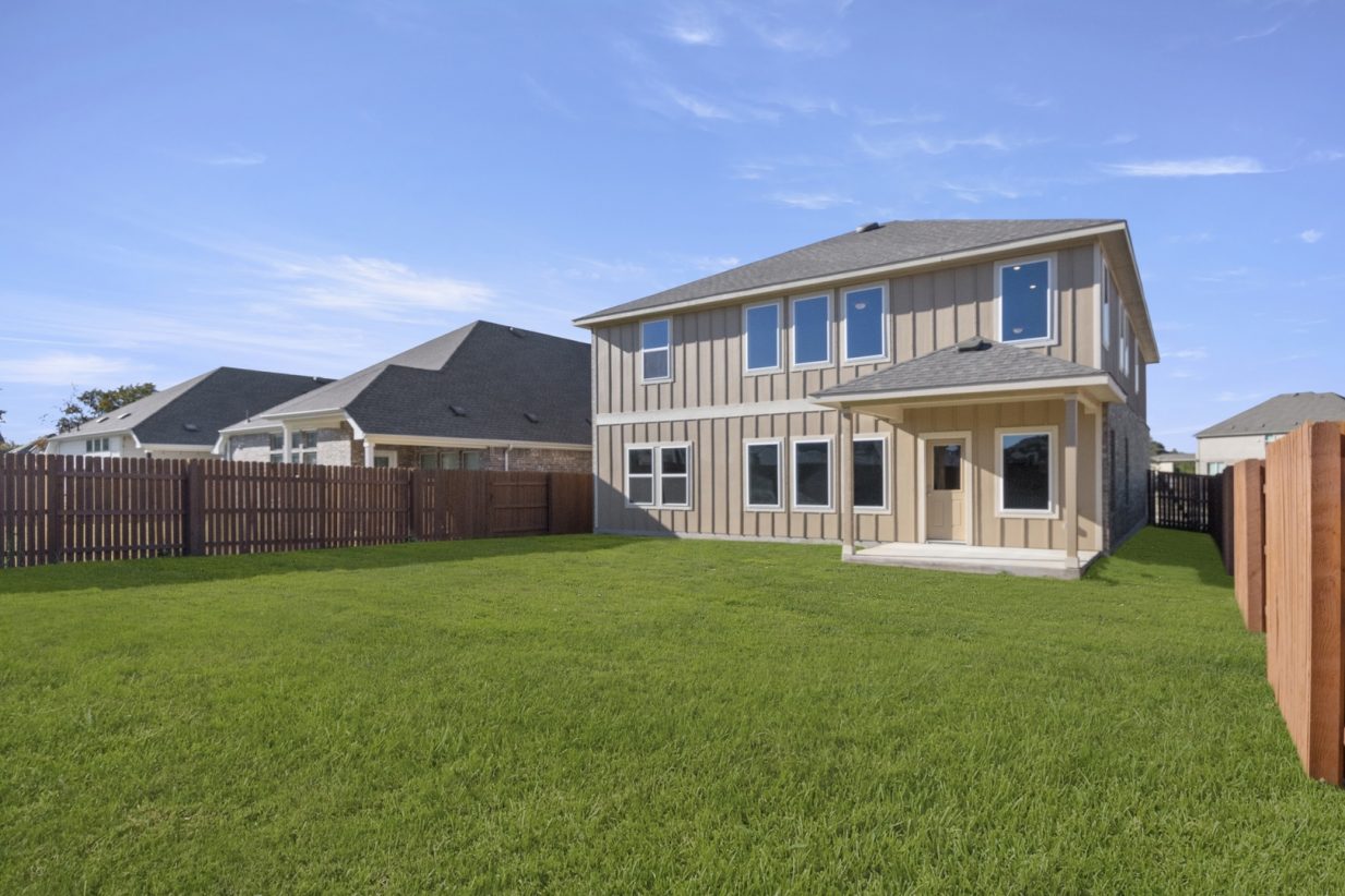 Image of the back exterior of a two story home with green grass, a wooden fence, and a blue sky