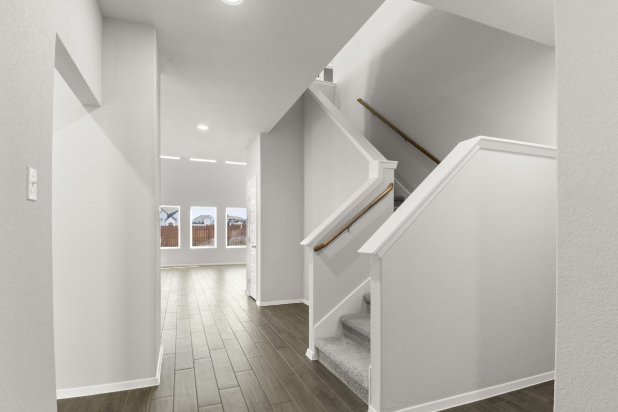 Image of a foyer with dark wood-like flooring and grey carpeted staircase leading upstairs