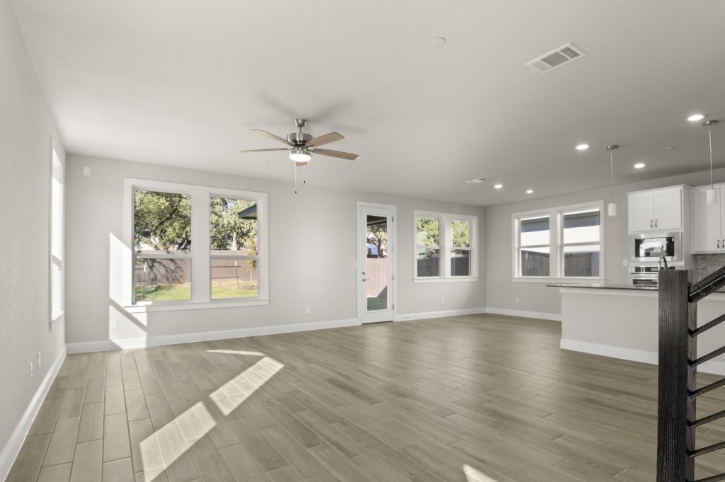 Image of a two story home living room with wood-like flooring and light grey painted walls with windows and a ceiling fan
