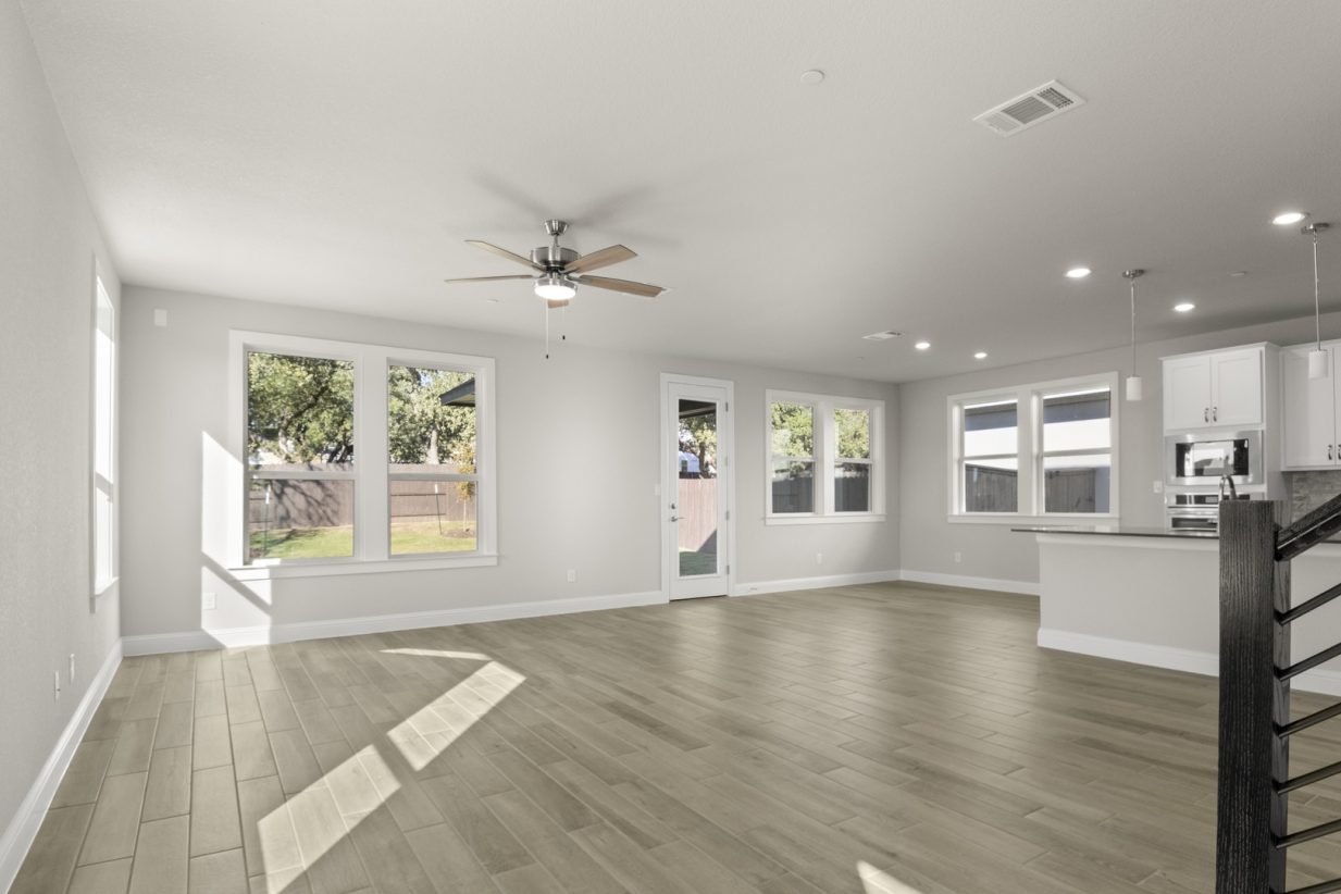 Image of a two story home living room with wood-like flooring and light grey painted walls with windows and a ceiling fan
