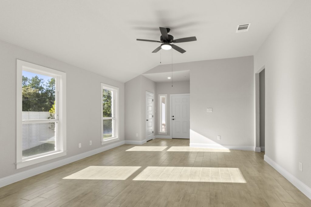 Image of a one story home living room with light wood-like flooring and light grey painted walls with two large windows and a ceiling fan