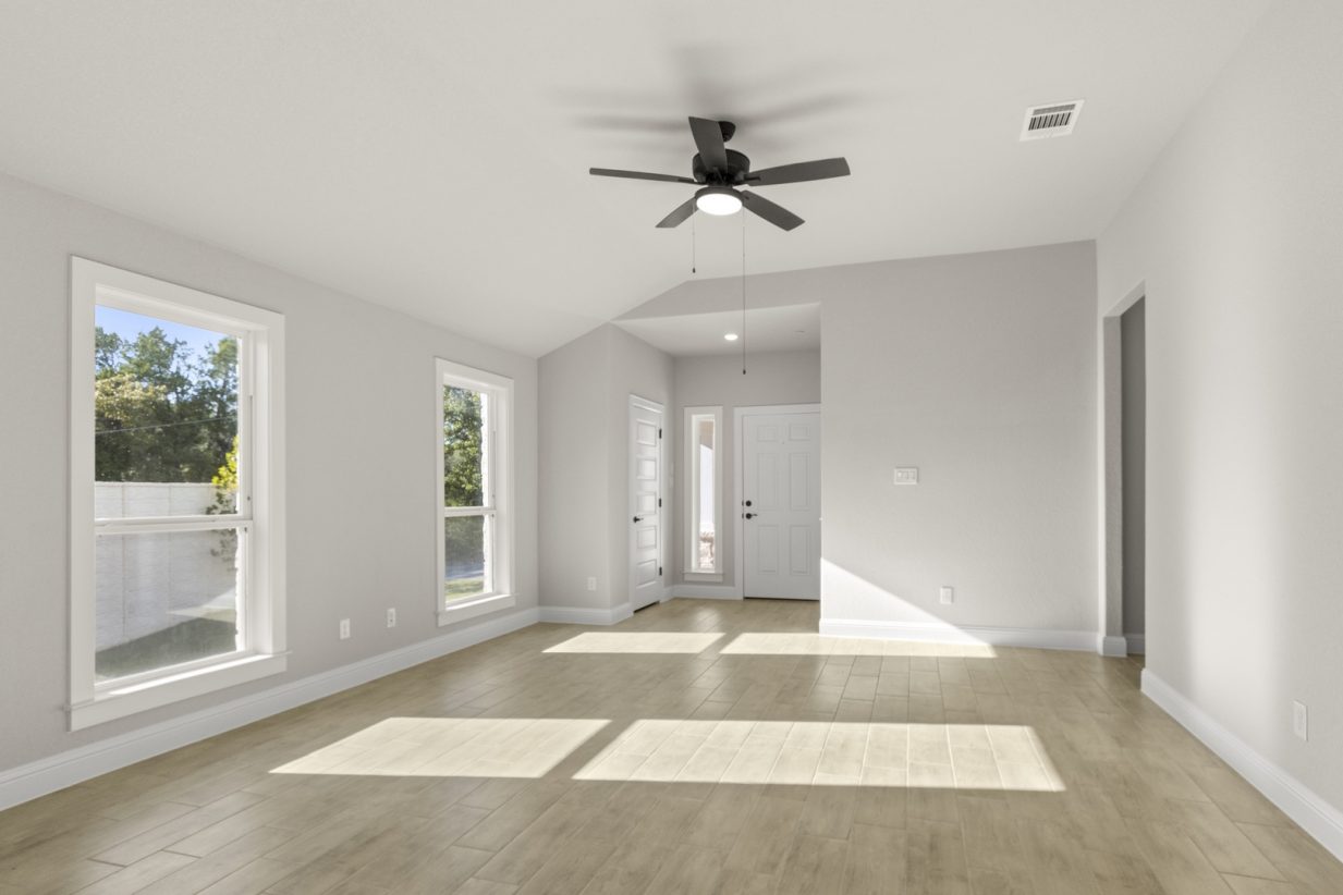 Image of a one story home living room with light wood-like flooring and light grey painted walls with two large windows and a ceiling fan