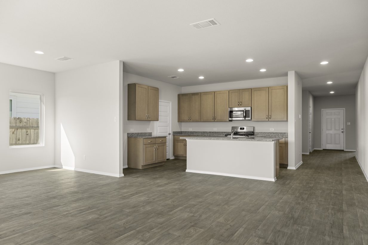 Image of home kitchen with light brown cabinets, center island, wood-look floors and white walls. Dining room on the left and entry way to front door on the right