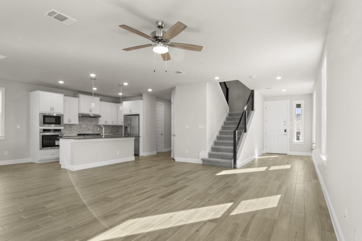 Image of a two story home living room with a grey carpeted staircase leading upstairs and a open layout with a kitchen