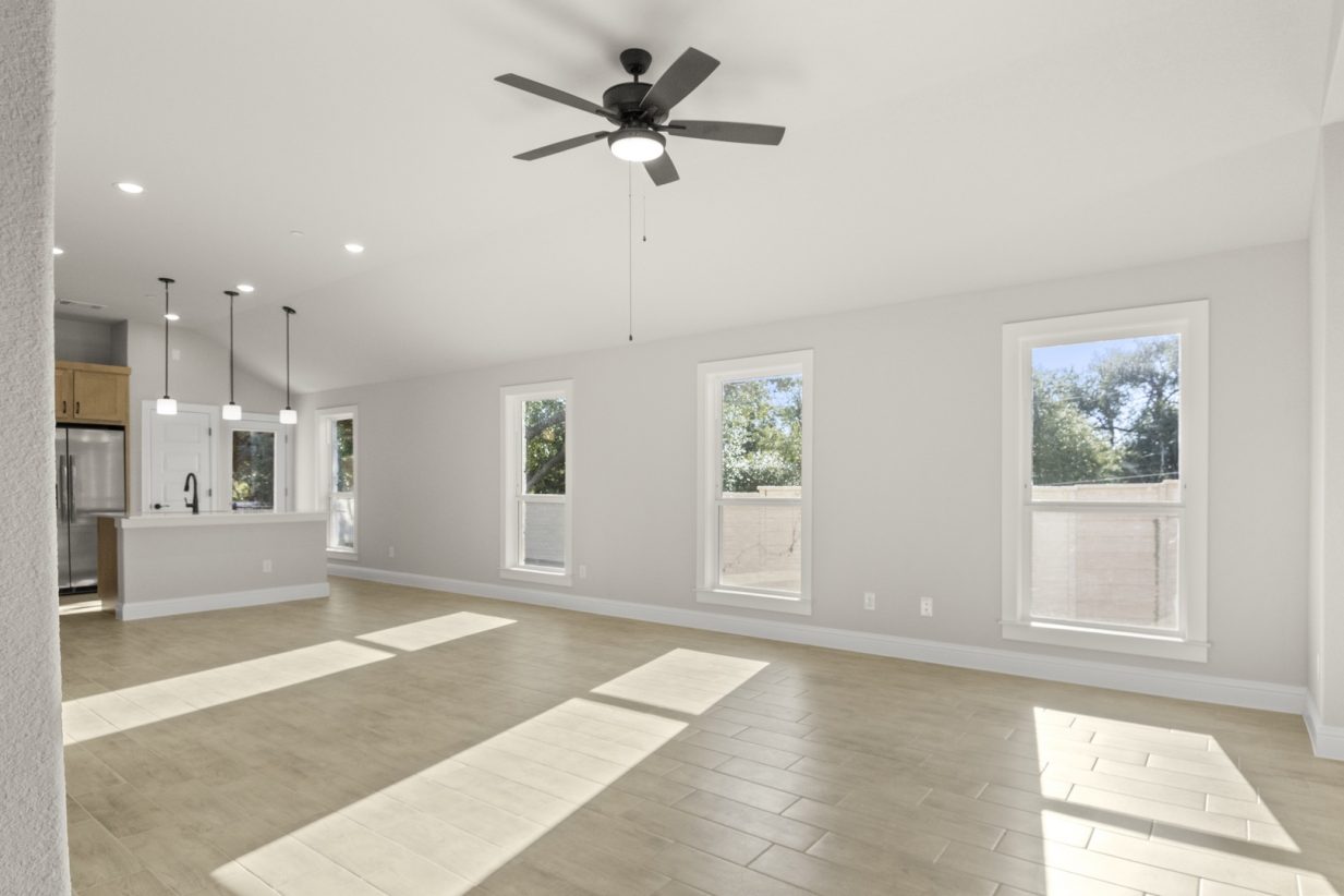 Image of a one story home living room with light wood-like flooring and light grey painted walls with two large windows and a ceiling fan
