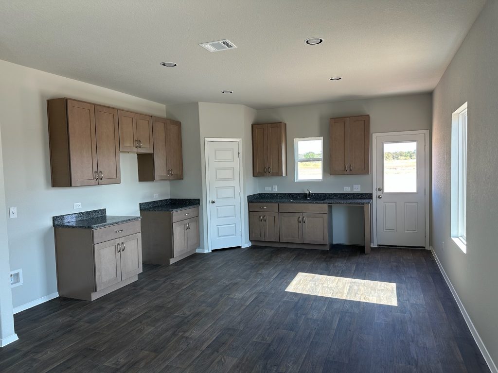 Image of home kitchen with light brown cabinets, wood-look floors, and window on wall, rear door, and over sink