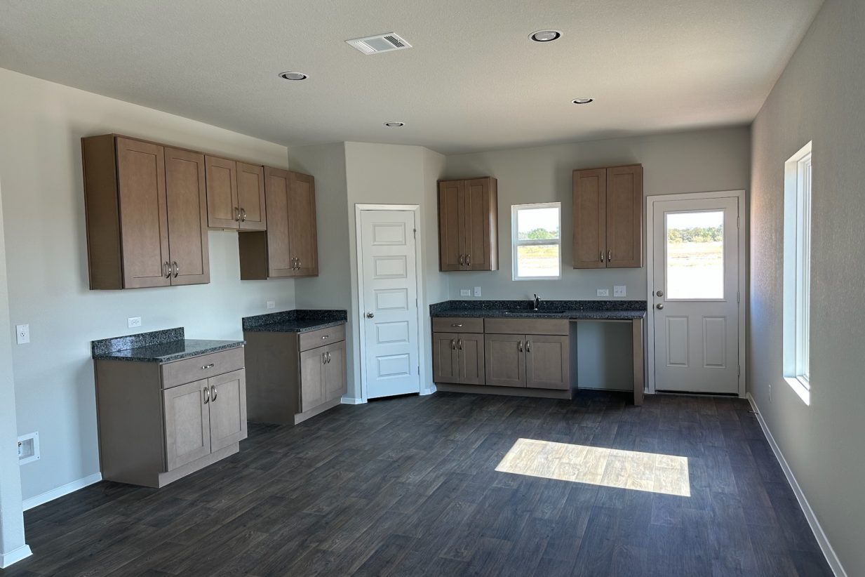 Image of home kitchen with light brown cabinets, wood-look floors, and window on wall, rear door, and over sink