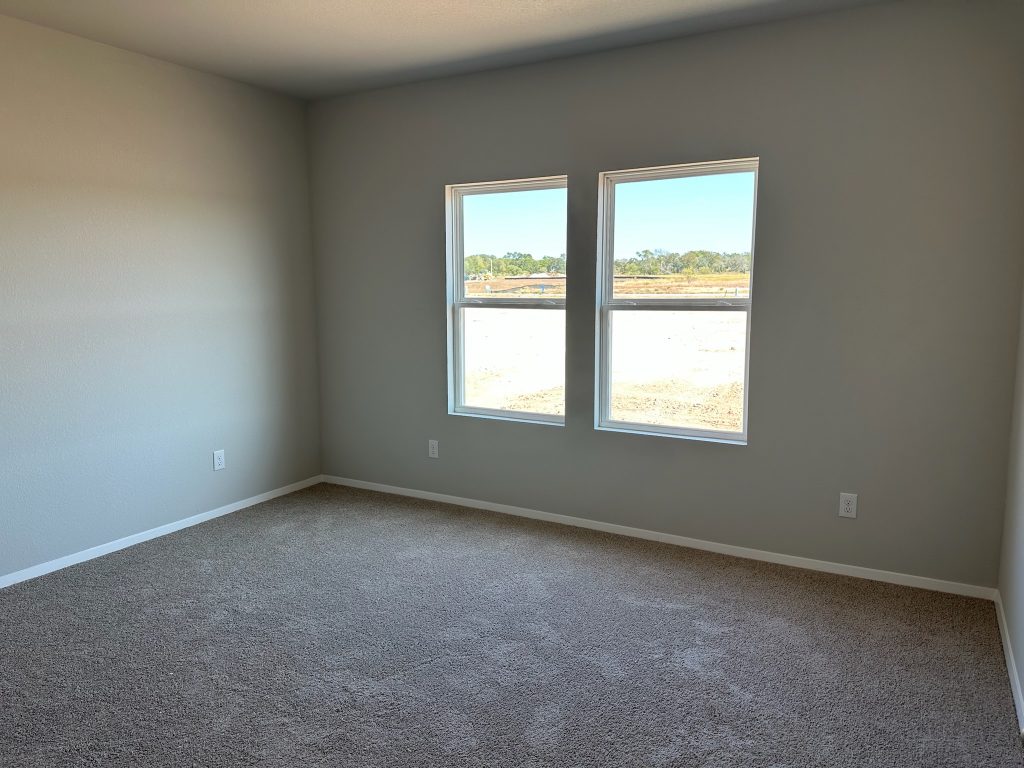 Photo of home primary bedroom with light carpet, white walls, and two windows