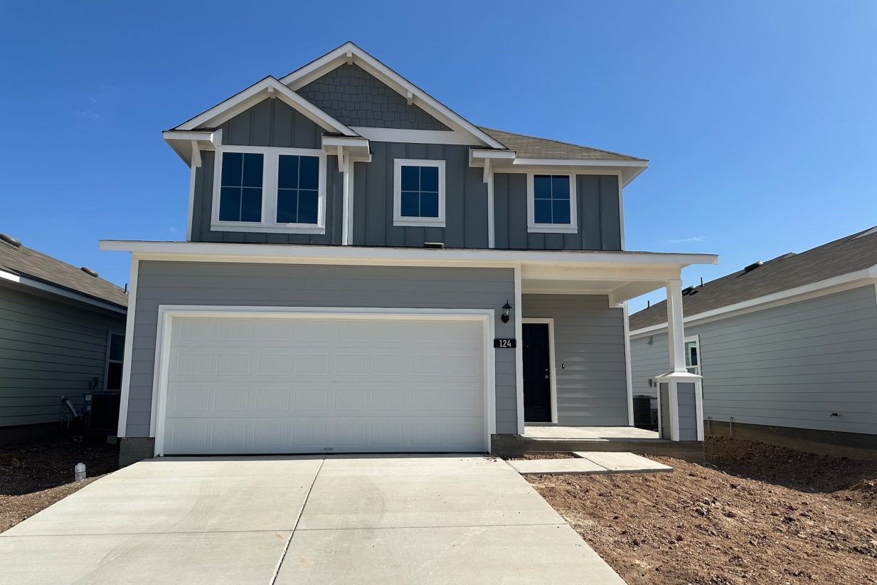 Image of two-story grey home with white garage door, driveway, and blue sky