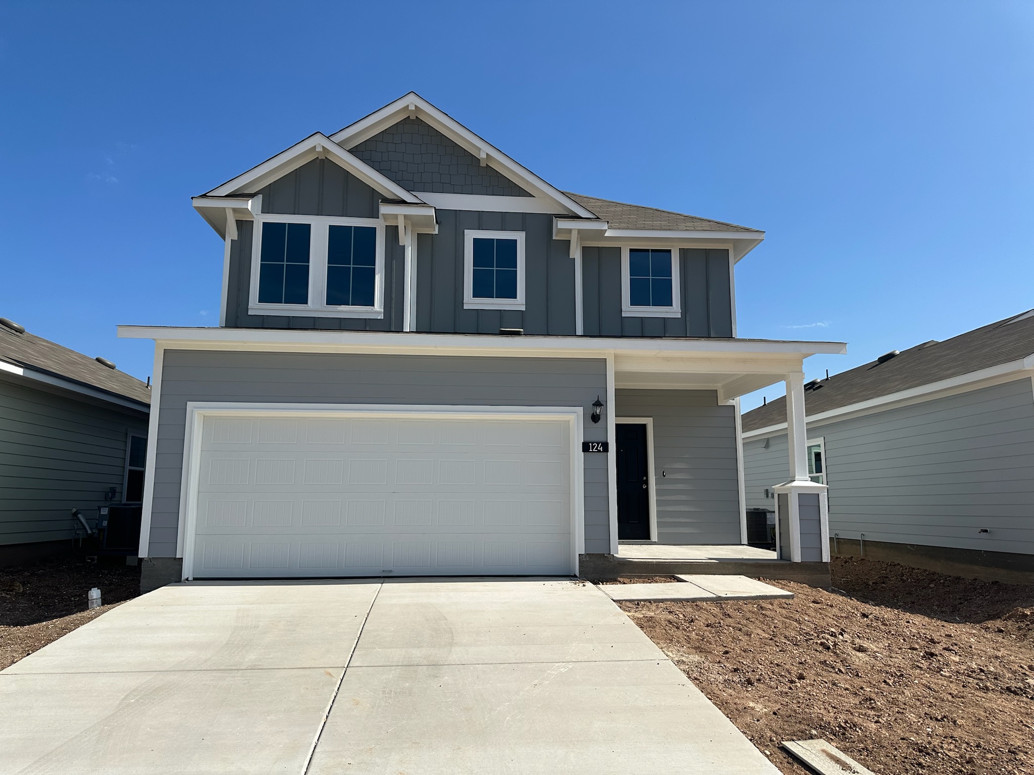 Image of two-story grey home with white garage door, driveway, and blue sky