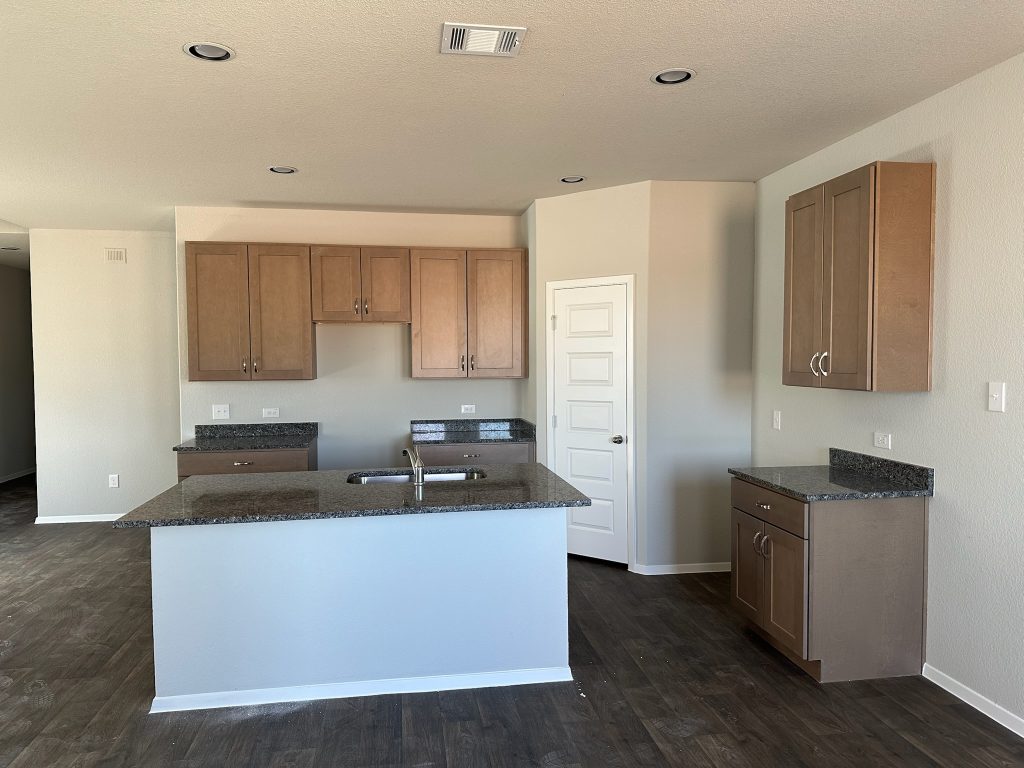 Image of home kitchen with light brown cabinets, center island, wood-look floors, and white walls