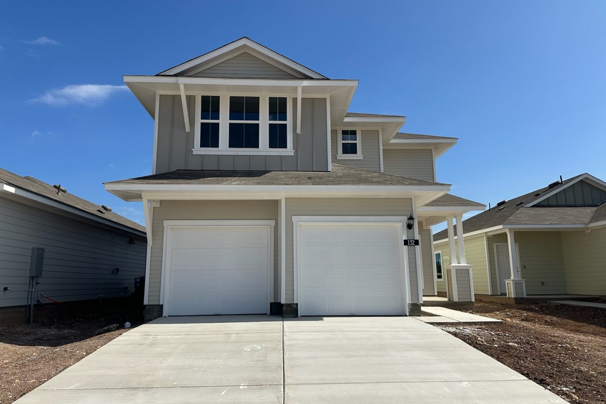 Image of two-story light tan home with two white garage doors, driveway, and blue sky