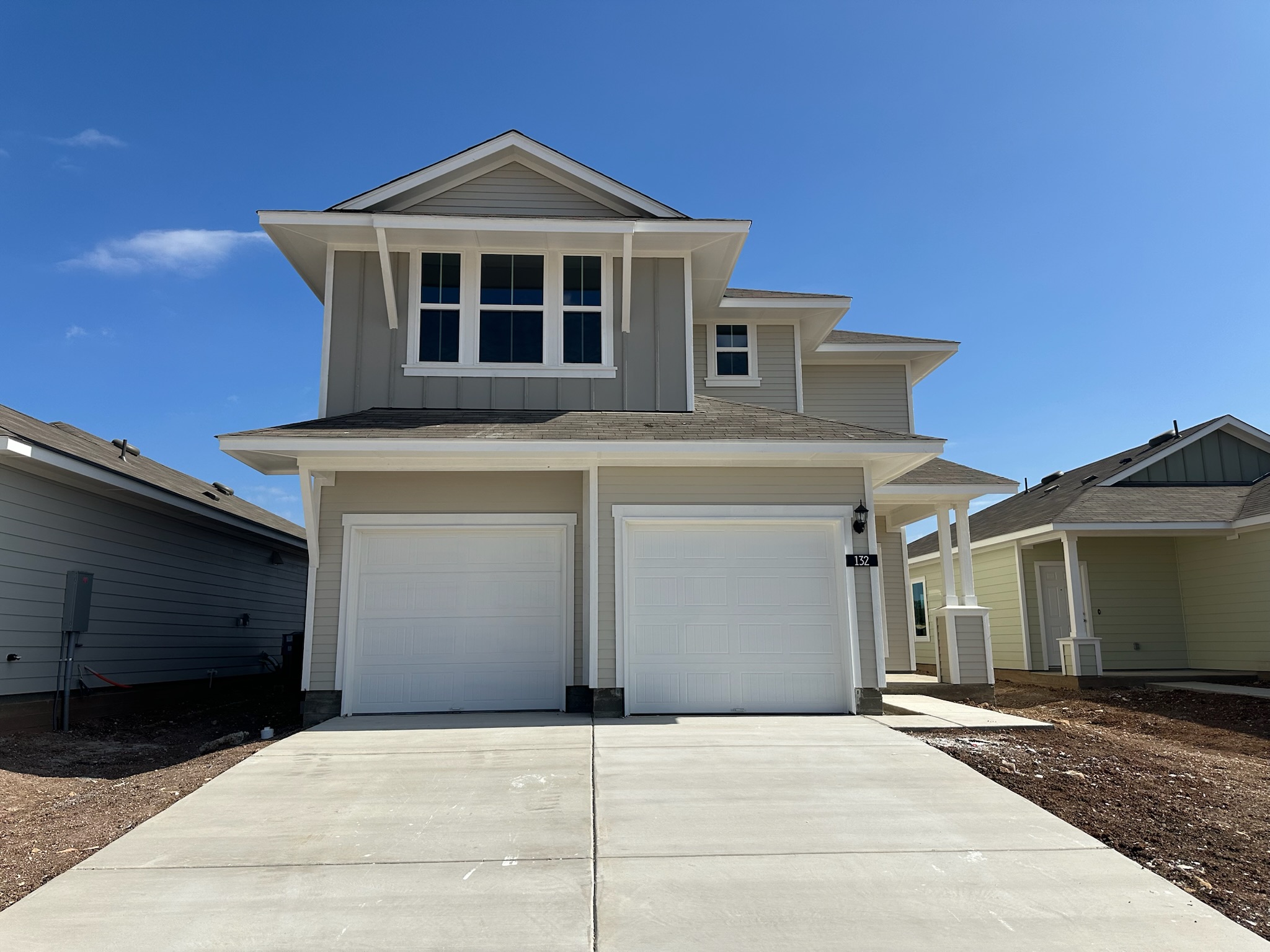 Image of two-story light tan home with two white garage doors, driveway, and blue sky