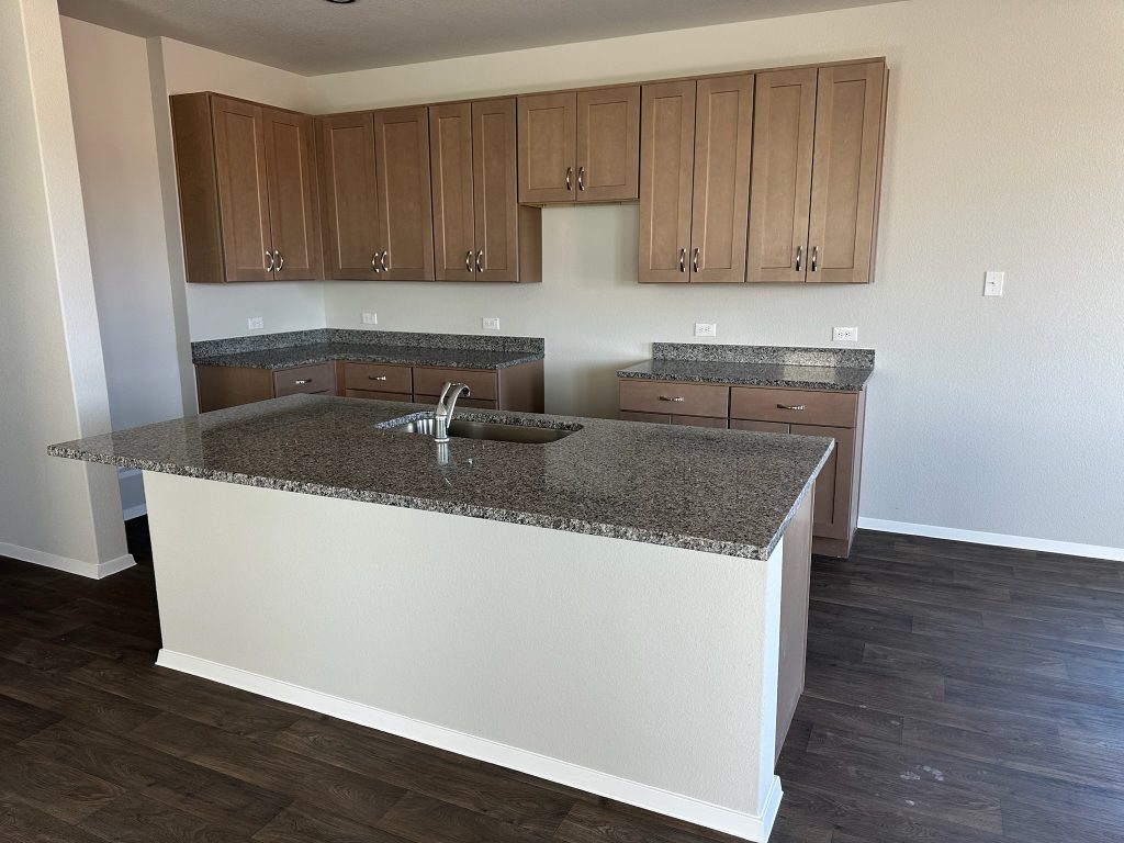 Image of home kitchen with light brown cabinets, center island, wood-look floors, and white walls