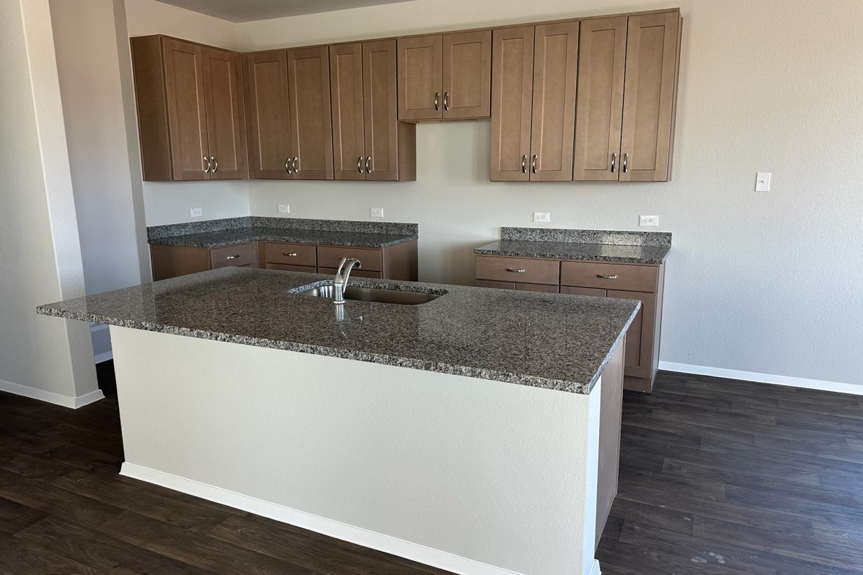 Image of home kitchen with light brown cabinets, center island, wood-look floors, and white walls