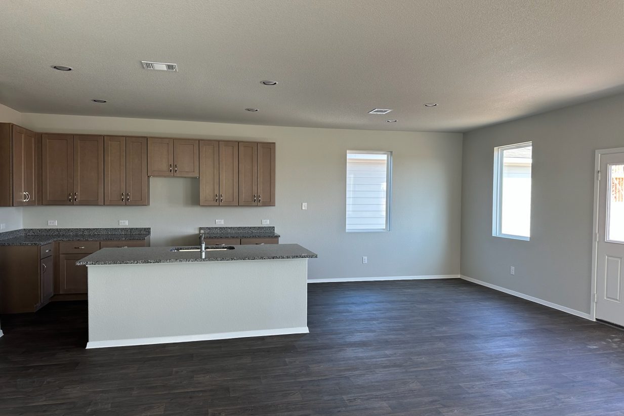 Image of home kitchen and dining room with light brown cabinets, center island, wood-look floors, and white walls with windows