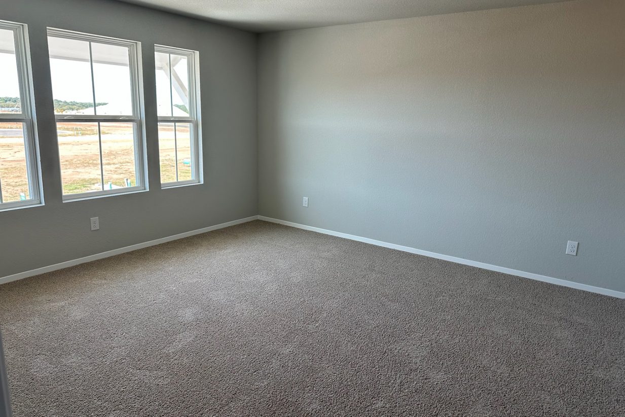 Image of home primary bedroom with light carpet, white walls, and windows