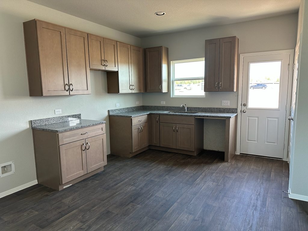 Image of home kitchen with light brown cabinets, wood-look floors, and window on rear door and over sink