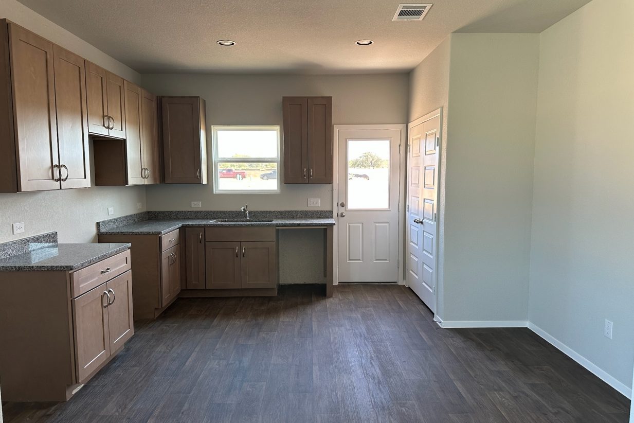 Image of home kitchen with light brown cabinets, wood-look floors, and window on rear door and over sink