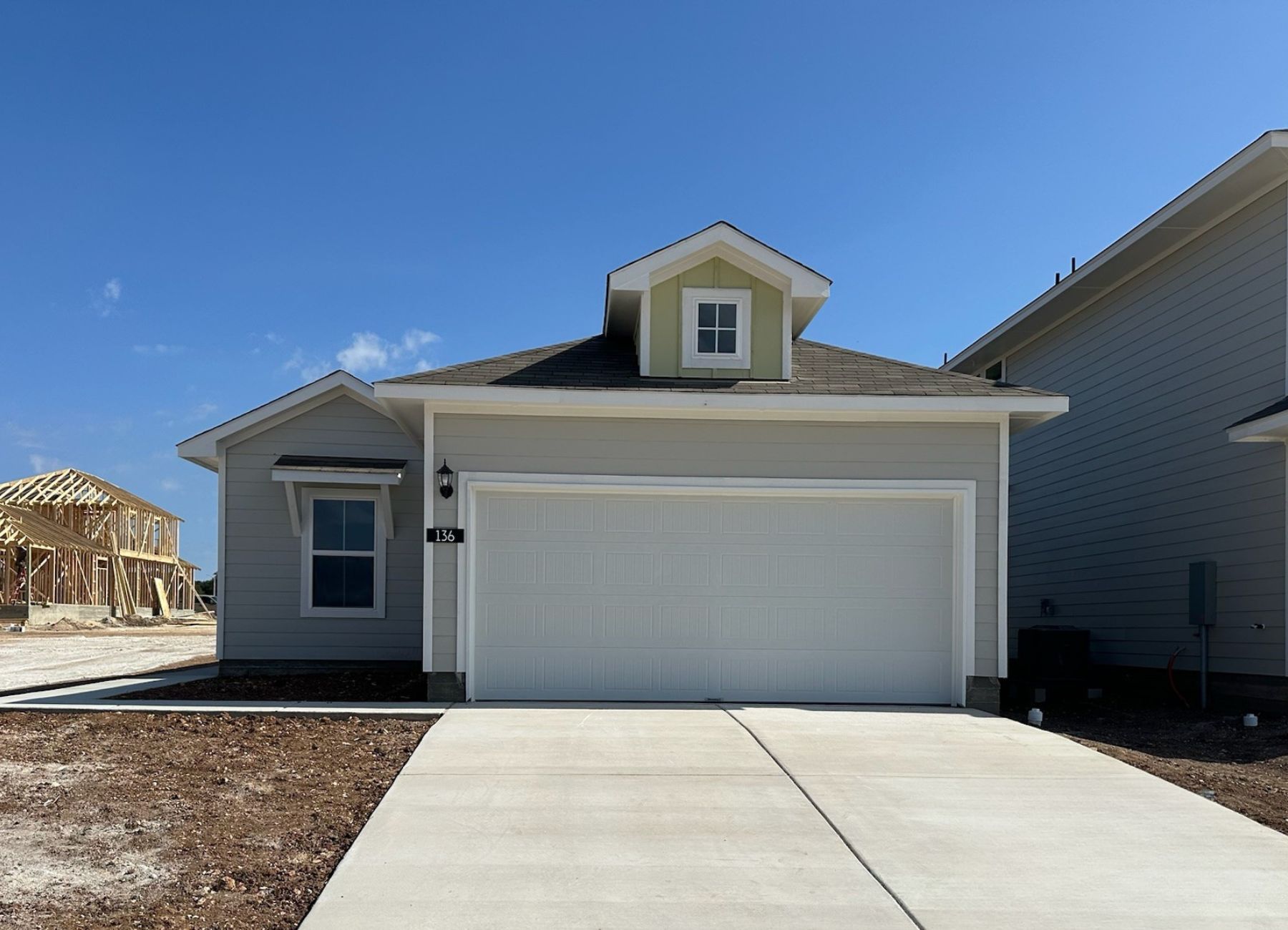Image of one story home with tan siding, yellow accent, and white trim and garage door