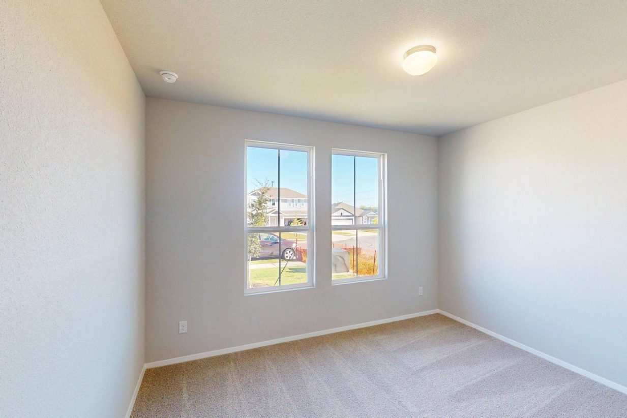 Image of a bedroom with tan carpeting and light grey walls with two windows