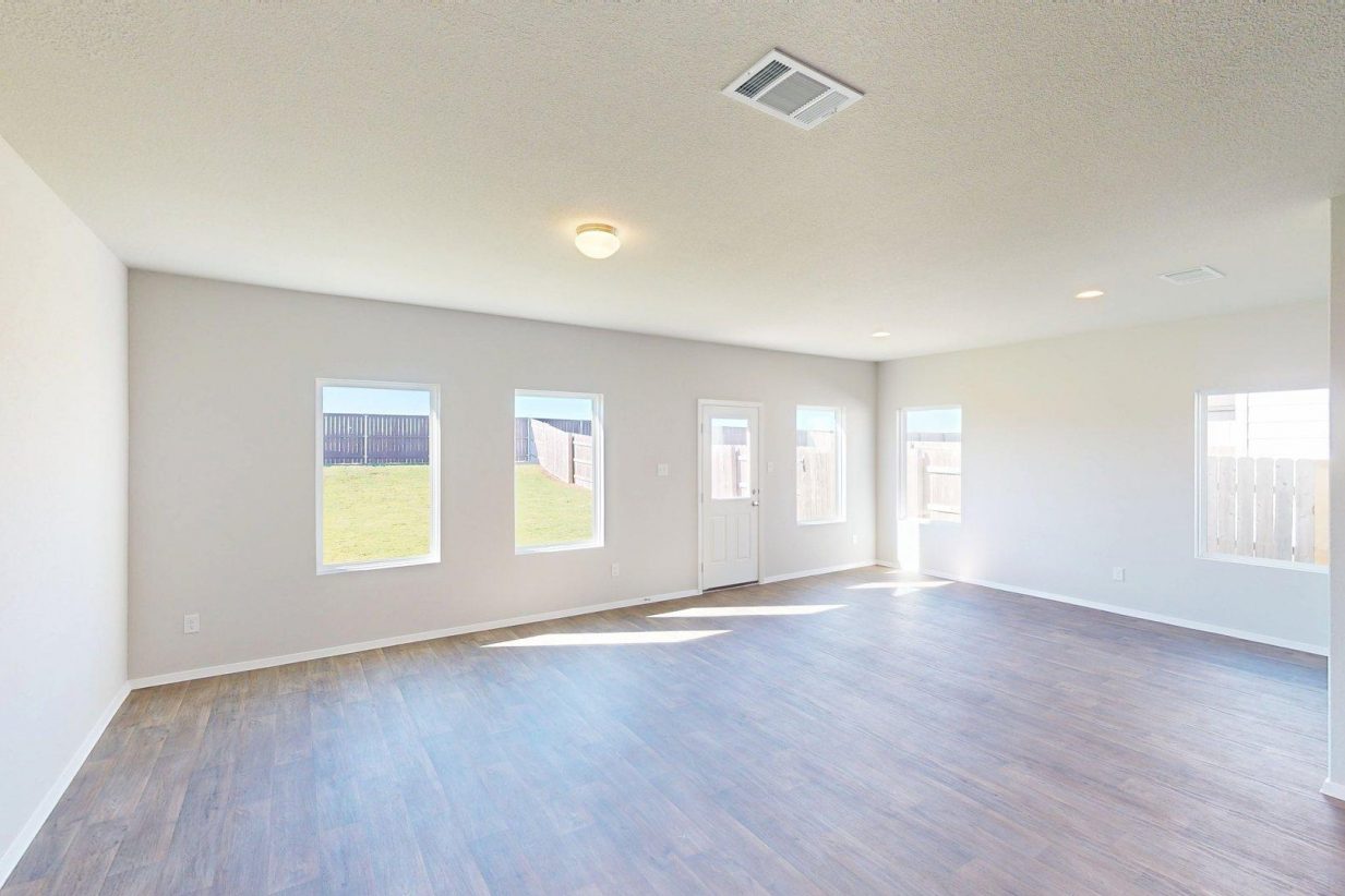 Image of a one story home living room with brown wood-like flooring and light grey painted walls with windows and natural lighting