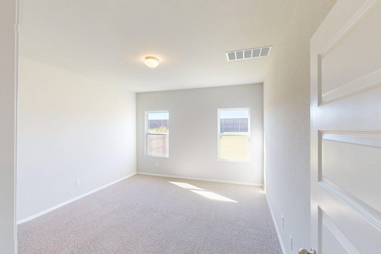 Image of a bedroom with tan carpeting and light grey walls with two windows