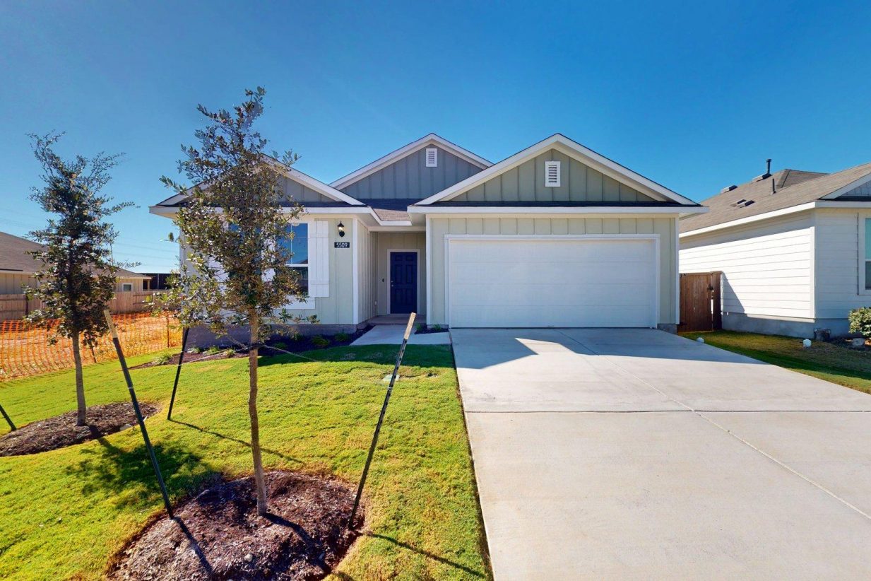 Image of the exterior of a one story home with a two car garage and cement driveway with green grass and a blue sky
