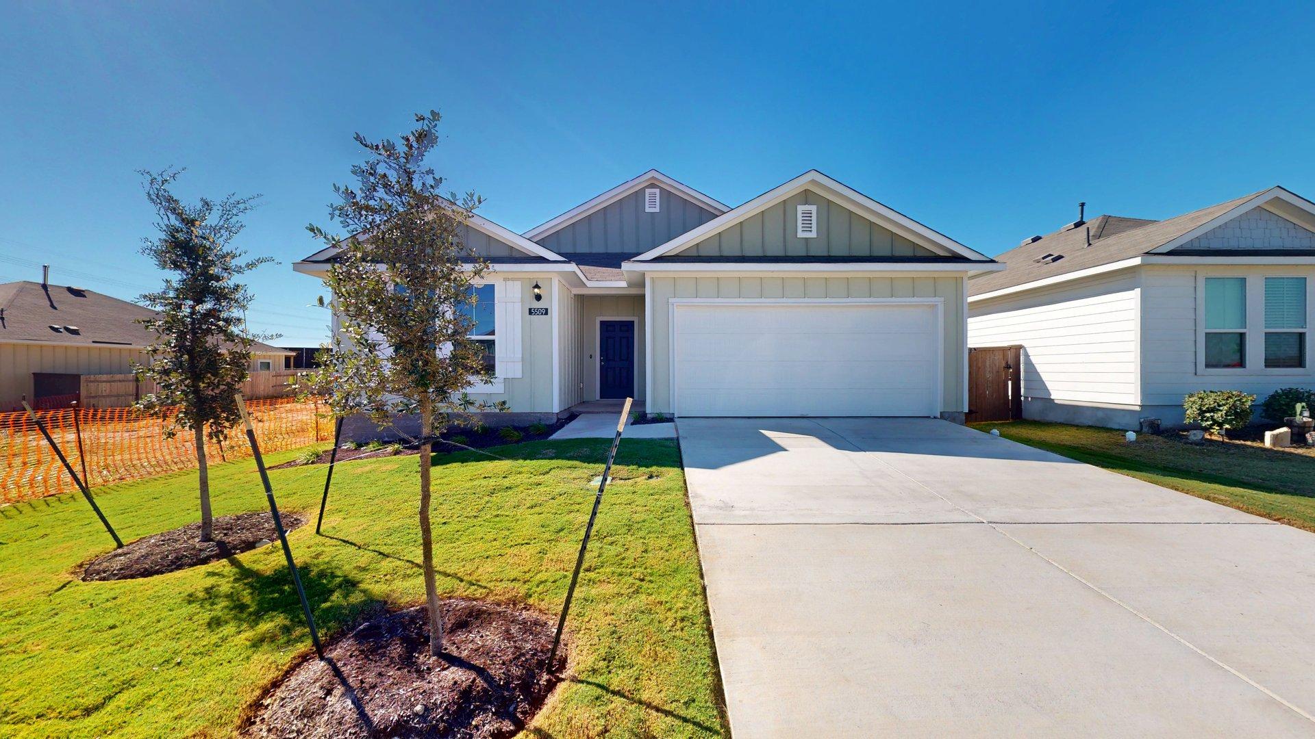 Image of the exterior of a one story home with a two car garage and cement driveway with green grass and a blue sky