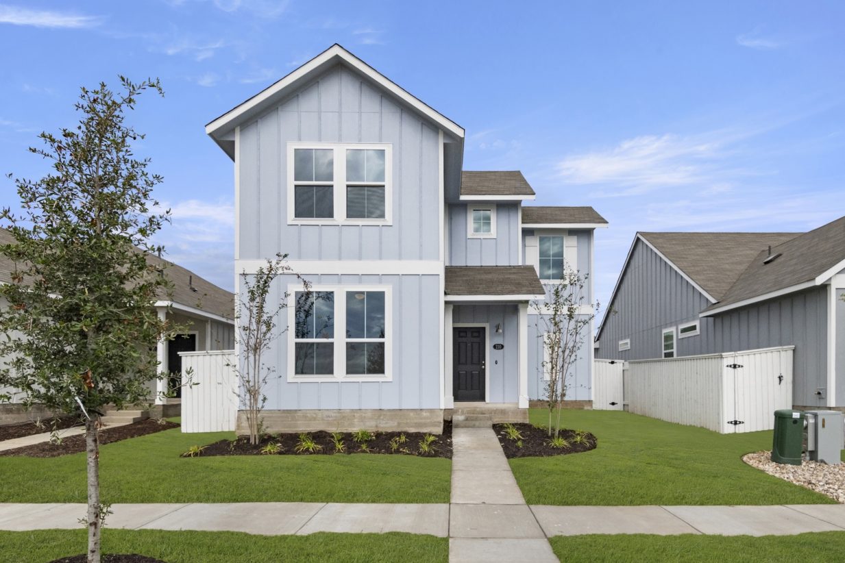 Image of the exterior of a blue two story home with a tree, green grass, and a blue sky