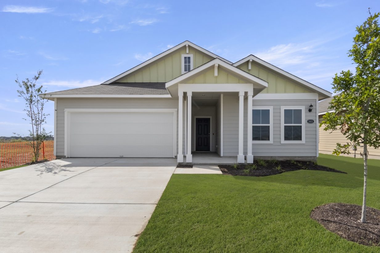 Image of front exterior of a single-story yellow house with white garage door, green grass landscape, and blue sky with clouds.