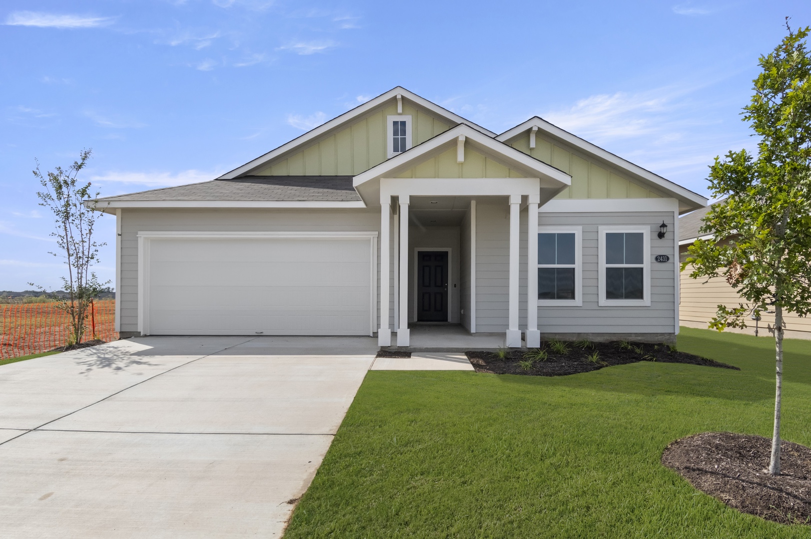 Image of front exterior of a single-story yellow house with white garage door, green grass landscape, and blue sky with clouds.
