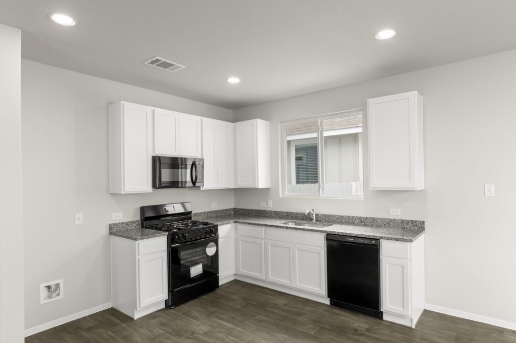 Image of a kitchen with white cabinets, black appliances, and a window above the sink