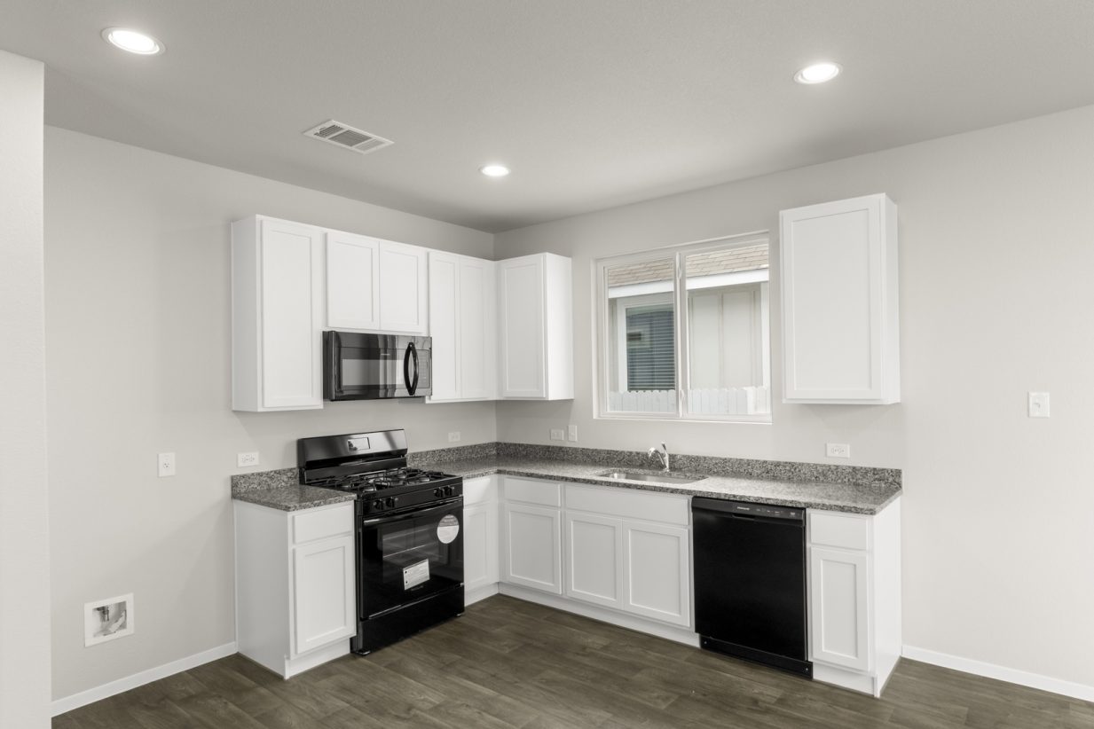Image of a kitchen with white cabinets, black appliances, and a window above the sink