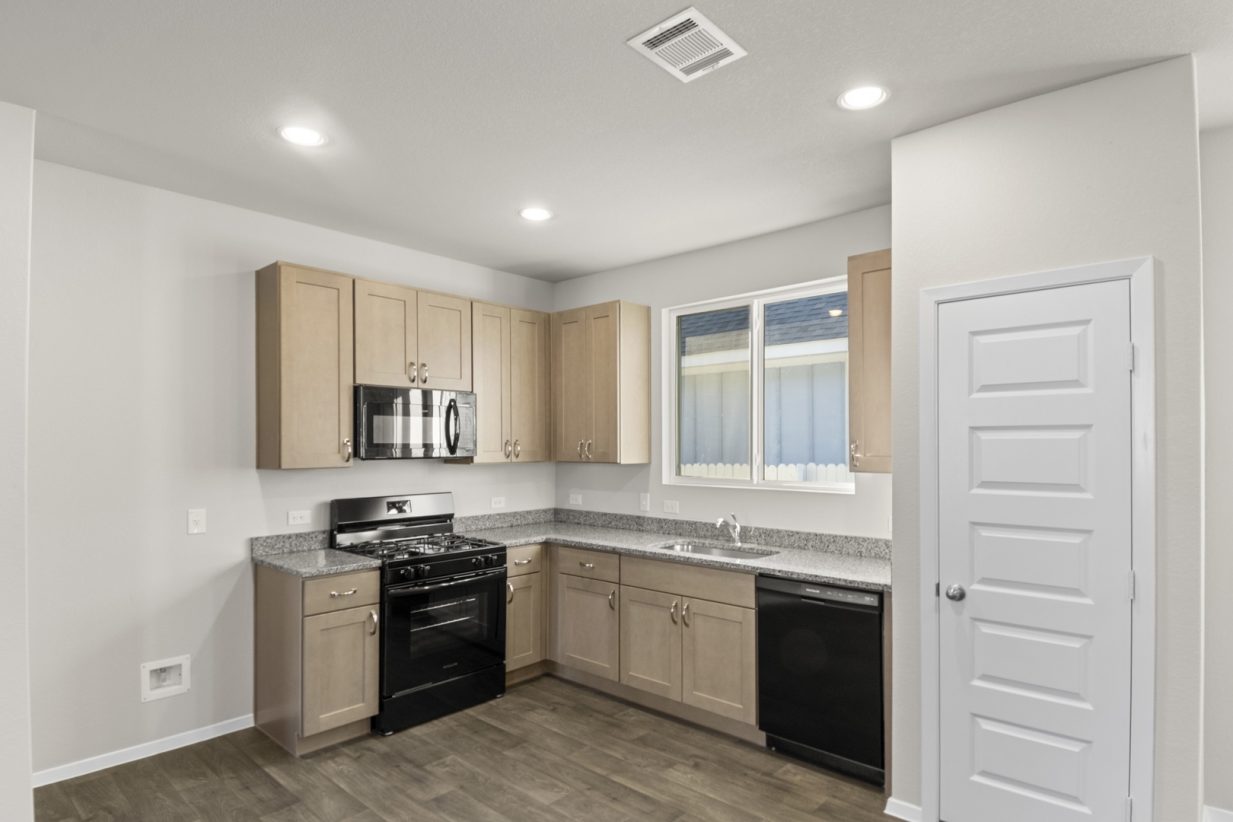 Image of a kitchen with brown cabinets and granite counter tops with black appliances and a window above the sink
