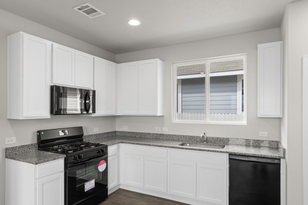 Image of a one story home kitchen with white cabinets and black appliances with a window over the sink