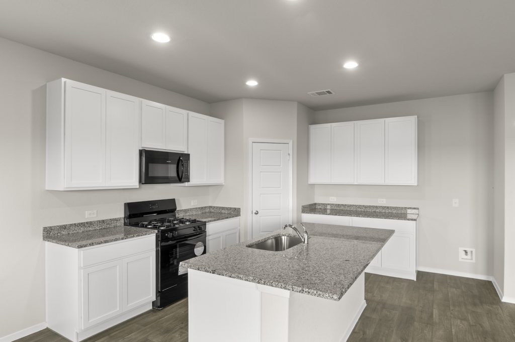 Image of a one story home kitchen with white cabinets and black appliances and a centered white island