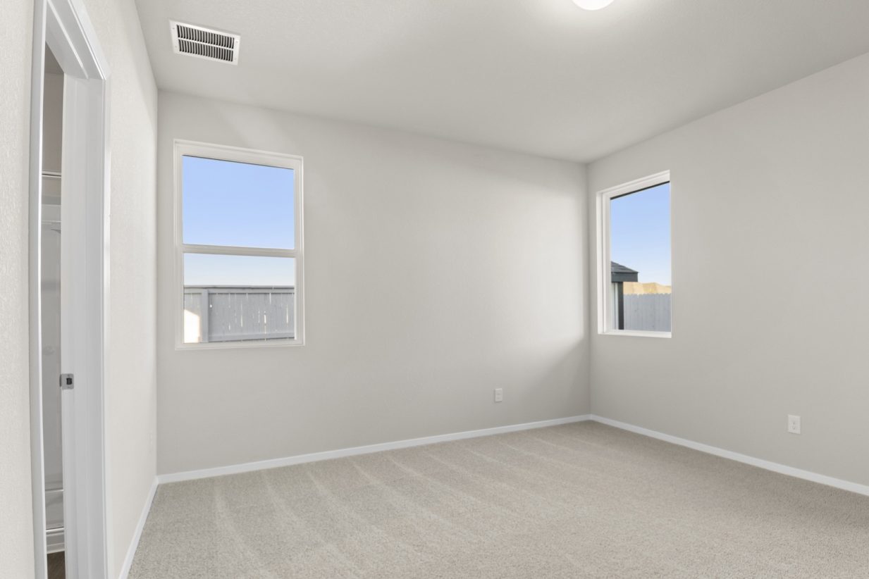 Image of a primary bedroom with tan carpeting and light grey painted walls with two windows