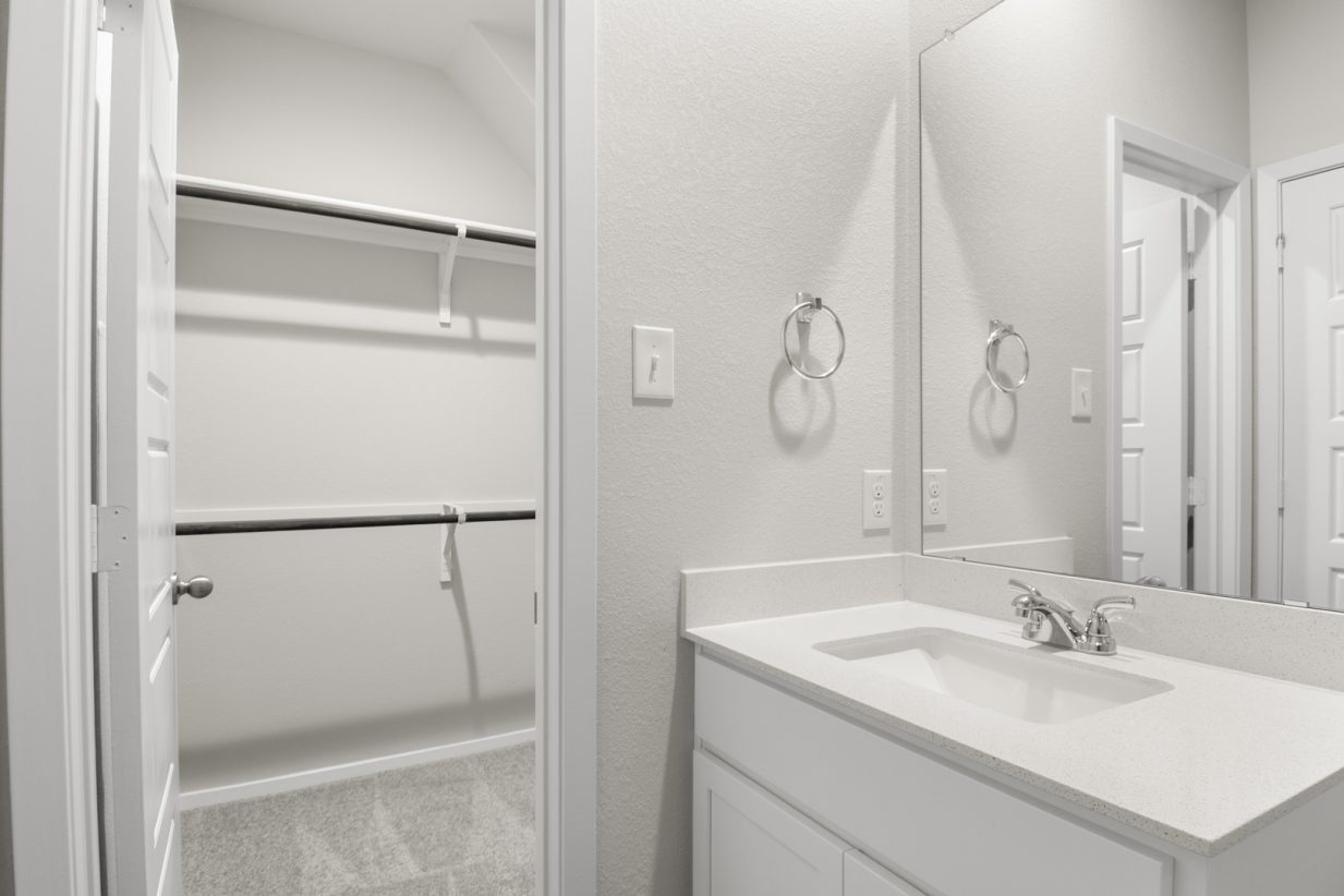 Image of primary bathroom with white cabinets and mirror with vanity and a walk in closet