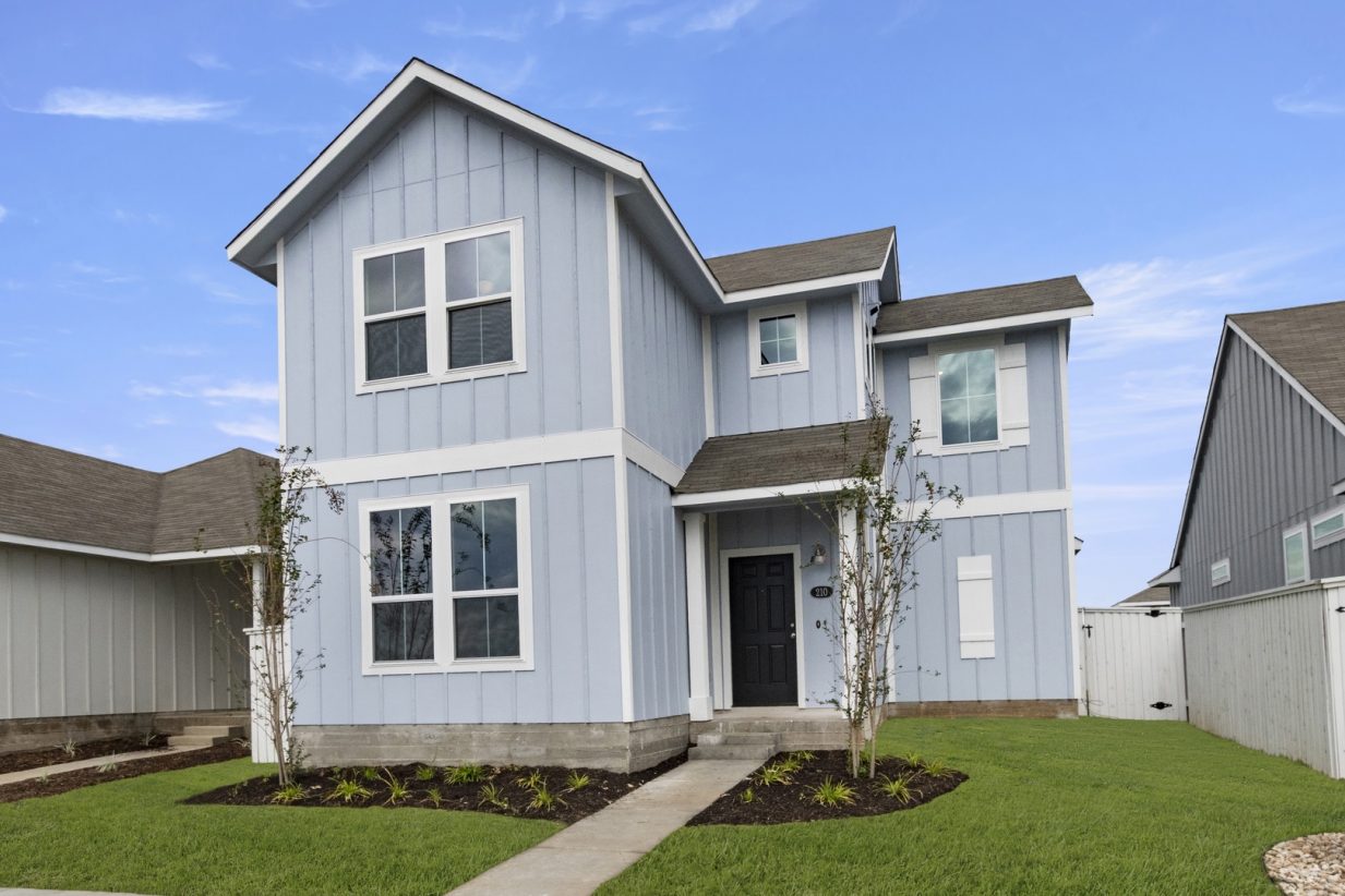 Image of the exterior of a blue two story home with a tree, green grass, and a blue sky