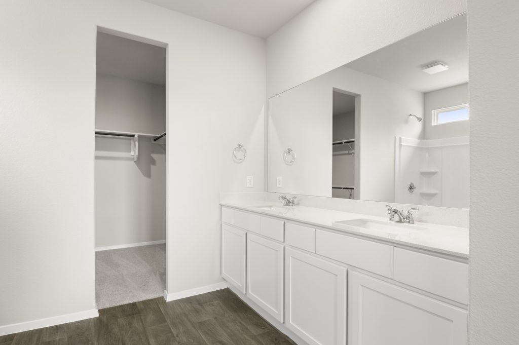 Image of primary bathroom with white cabinets and mirror with a two sink vanity and walk in closet