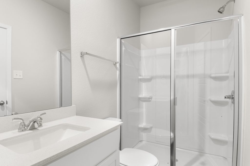 Image of primary bathroom with a walk in shower, white cabinets and a mirror with vanity
