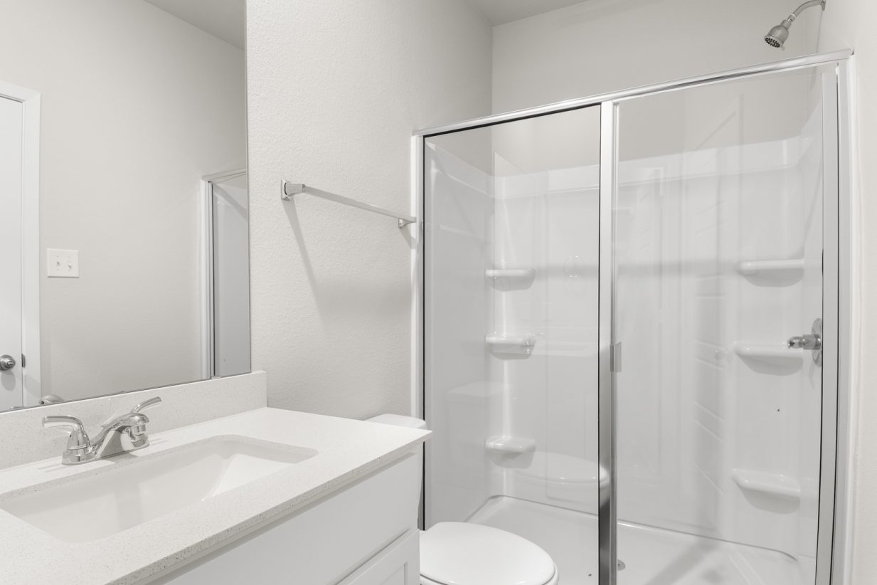 Image of primary bathroom with a walk in shower, white cabinets and a mirror with vanity
