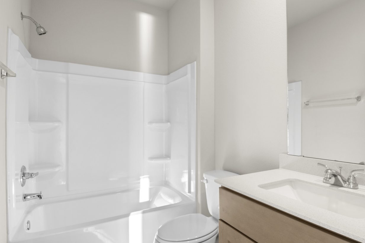 Image of a bathroom with brown cabinets and a white vanity with a white vinyl shower and tub