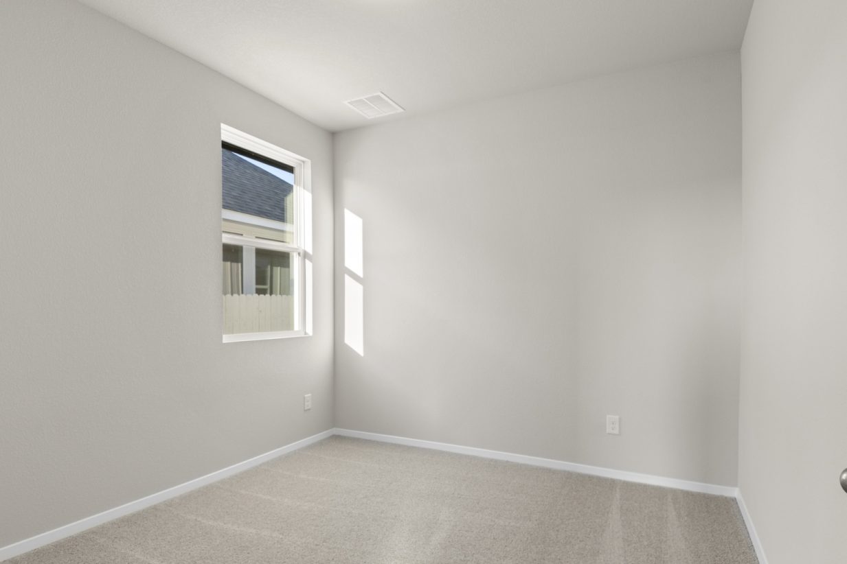 Image of a bedroom with tan carpeting and light grey walls with a window